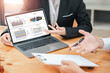 © Satori Studio - Two business professionals discussing financial charts and graphs displayed on a laptop during a meeting, focusing on data analysis and strategy.