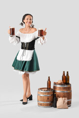 Wall Mural - Beautiful mature happy Octoberfest waitress with barrels, mugs of beer and pretzels on grey background