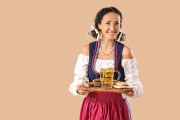 Wall Mural - Beautiful mature happy Octoberfest waitress with mug of beer and snacks on beige background