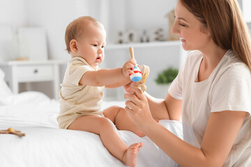 Wall Mural - Beautiful young happy mother with cute little baby and rattles sitting in bedroom at home