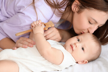 Sticker - Beautiful young mother kissing her cute little baby with rattle while lying in bedroom at home