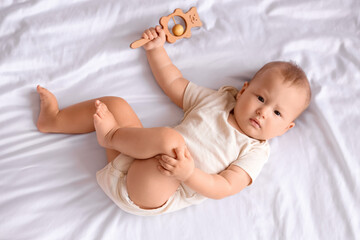 Poster - Cute little baby with rattle lying on bed in room at home, top view