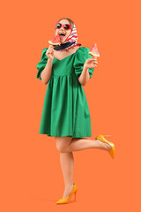 Wall Mural - Beautiful young happy woman with pieces of fresh watermelon on sticks against orange background