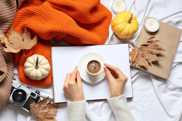 Wall Mural - Female hands with cup of tasty pumpkin coffee, books and warm sweaters on bed at home, top view