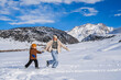 © alexkoral - Mom and son running on a snow-covered slope against the backdrop of a mountain landscape in winter.