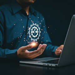 Wall Mural - A person wearing a blue shirt, laptop computer in front of them, hands holding a floating holographic gear icon with a medical cross symbol, digital healthcare technology concept, dark background with