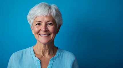 Wall Mural - A senior woman with short, silver hair beams warmly, showcasing happiness against a vibrant blue backdrop, creating an inviting and joyful atmosphere