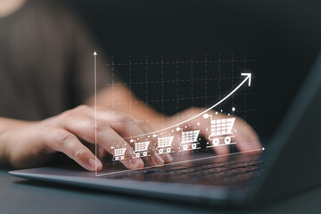 Sale growth concept. Businessman use laptop with graph of increase in sales volume with shopping cart on virtual screen for ecommerce growth.