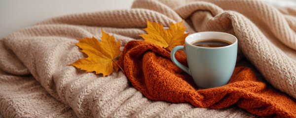 A cup of coffee, a gray plaid or sweater and fall maple yellow leaves. Cozy warm composition for fall home decor, mood board, poster, card or banner with copy space. Autumn hygge atmosphere.