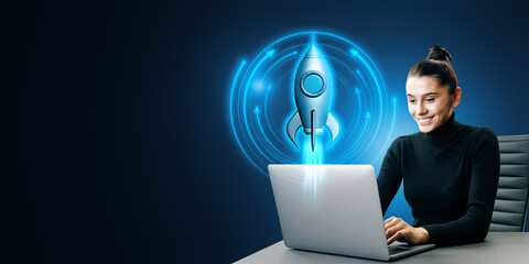 Poster - Attractive young european businesswoman using laptop at desk with glowing rocket on blue background with mock up place. Digital transformation, start up and boost concept.