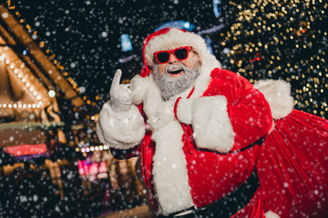 Poster - Portrait of careless brutal fat aged santa carry gifts sack hand fingers show heavy metal symbol evening tree lights street outdoors