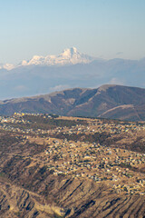 Sticker - Mount Mkinvartsveri Kazbek in the morning sun covered with snow. Village houses on the hill in the foreground