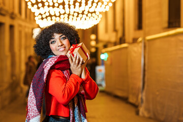 Young woman holding christmas gift on decorated street