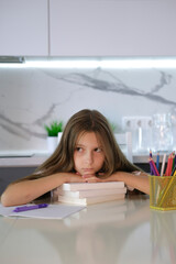 Portrait of tired, sad girl falling asleep at table while doing her homework. Child concentrates and focuses on task for elementary school. Back to school. Homeschooling concept. Vertical image.