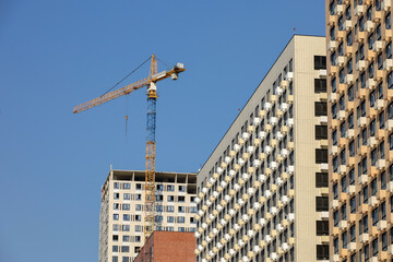 Wall Mural - Tower crane and unfinished buildings on background of blue sky. Housing construction, apartment blocks in city