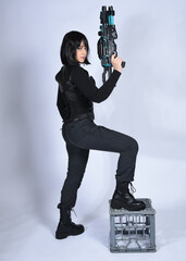 Poster - Full length portrait of beautiful black female model with short black hair wearing sci fi futuristic dystopian leather bodysuit costume. Standing pose holding gun weapon, isolated white studio backgro