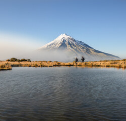 Couple hiking Pouakai circuit. Snow-capped Mt Taranaki in the background. New Zealand.