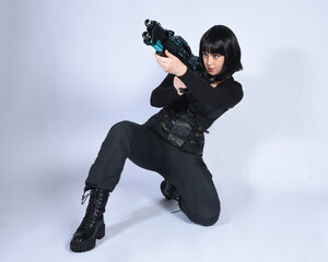 Poster - Full length portrait of beautiful black female model, black hair wearing sci fi futuristic dystopian leather bodysuit costume. sitting pose, holding  gun weapon, isolated white studio background.