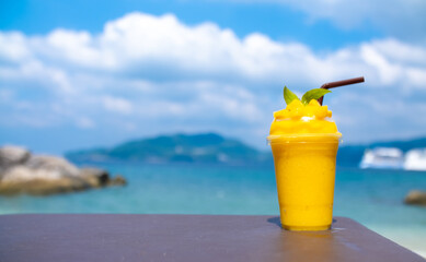 Smoothie made from fresh mango fruits against the backdrop of a seascape. Fruit and yoghurt ice cream decorated with leaves. Glass of tropical dessert close-up.