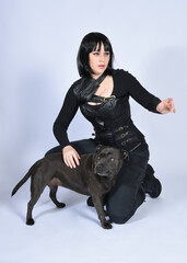 Poster - Full length portrait of beautiful black female model wearing sci fi futuristic dystopian leather bodysuit costume, with animal dog pet companion. sitting pose, isolated white studio background.