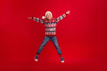 Wall Mural - Full body photo of cute little boy jumping star pose celebrate christmas wear knitwear sweater isolated on red color background