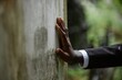 © Seventyfour - Close up on hand of Black man grieving over loss of loved one touching weathered memorial monument covered moss at grave at cemetery, copy space
