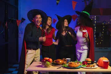 Wall Mural - Dinner and group of people celebrating together at Halloween party. Friends are happy and celebrating with food, wine and friendship of love and cheers of champagne at the event.