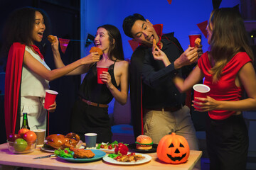 Wall Mural - Dinner and group of people celebrating together at Halloween party. Friends are happy and celebrating with food, wine and friendship of love and cheers of champagne at the event.