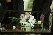 © Seventyfour - Cropped shot of unrecognizable people placing white lilies on memorial stone slab wet from rain to commemorate deceased person at cemetery, copy space