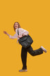 © somemeans - Young woman is running late holding her shoulder bag over a yellow background