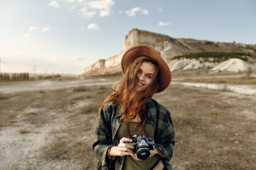 Woman in hat capturing scenic beauty of mountainous field with camera