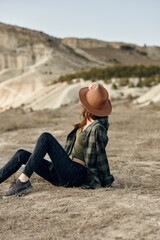 Wall Mural - Serene woman in hat sitting in field with majestic mountains in background