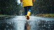 © Chatchanan - A person in a yellow raincoat and boots splashing through puddles on a deserted road