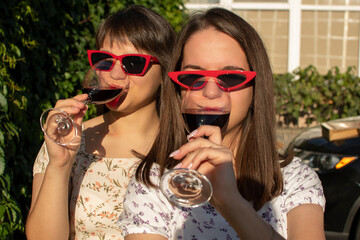 Wall Mural - Portrait of a two young woman in sunglasses drinking wine