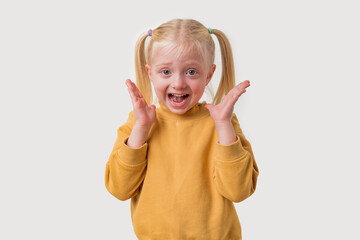 Portrait of a cute happy screaming little girl with blond hair wearing a yellow sweater.