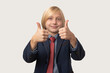 © somemeans - Young Caucasian boy with blond hair in suit and red tie shows thumbs up and smiles broadly, isolated over white background.
