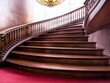 © ManitaSr - Elegant wooden staircase with a graceful curve and ornate railing, illuminated by a stunning chandelier above.
