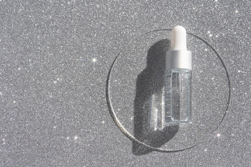 Transparent serum bottle with dropper on sparkling silver surface highlighting modern skincare and beauty essentials with glittering aesthetic appeal