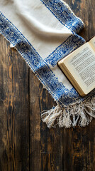 A tallit and prayer book are elegantly placed on rustic wooden table, creating serene atmosphere for reflection and spirituality. intricate design of tallit adds touch of tradition