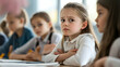 © Komkrit - A young girl in a school uniform sitting at a desk in class, one hand on her stomach, her face tense with discomfort, as classmates around her continue working
