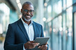 © wolfhound911 - Middle-aged Black businessman happily using a tablet in a bright, modern office with artistic touches.