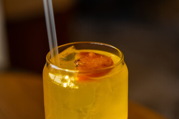 Close-up side view of drinking glass with orange fruit lemonade and drinking straw on wooden table in restaurant or cafe. Soft focus. Cold drinks theme.