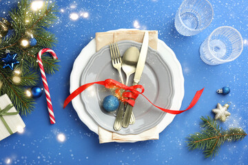 Beautiful Christmas setting with plates, elegant cutlery and festive decor on blue table, flat lay. Bokeh effect