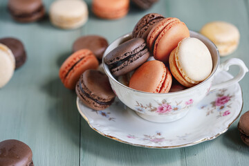 Wall Mural - Antique teacup filled with a variety of fresh French chocolate and orange macarons. Selective focus with blurred foreground and background.