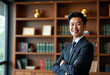 © Graphic Dude - Confident Asian businessman lawyer arms crossed smiling portrait in office bookshelf background success leadership professional entrepreneur executive management corporate finance legal advisor