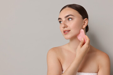 Wall Mural - Beautiful young woman doing facial massage with gua sha tool on grey background, space for text