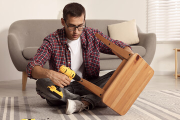 Canvas Print - Man repairing wooden stool with electric screwdriver indoors