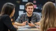 © fotofabrika - A young man smiles and engages in a group discussion with two peers in a classroom during a collaborative learning session