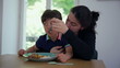 © Marco - Mother feeds young boy at dining table, holding him gently while he eats. The boy enjoys his meal in a cozy, sunlit room, illustrating a nurturing and caring family moment