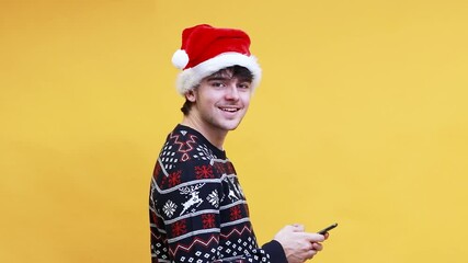 Poster - portrait of young man with santa claus hat typing on mobile phone and looking at camera